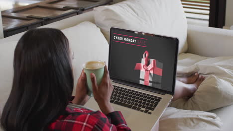Biracial-woman-on-couch-with-coffee-using-laptop-for-online-shopping,-slow-motion