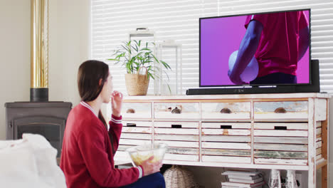 Caucasian-woman-watching-tv-with-african-american-male-rugby-player-with-ball-on-screen