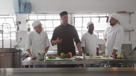 Diverse-male-chef-instructing-group-of-trainee-male-chefs-in-kitchen,-slow-motion