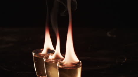 Two-shot-glasses-with-a-clear-liquid-are-ablaze-with-flames,-set-against-a-dark-background