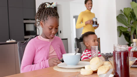 Niño-Afroamericano-Comiendo-Y-Niña-Usando-Smatphone-En-La-Cocina,-Cámara-Lenta