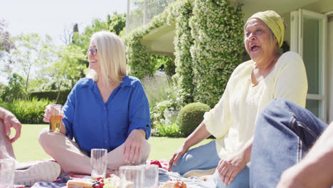 Happy-biracial-senior-woman-talking-with-diverse-friends-at-a-picnic-in-sunny-garden,-slow-motion
