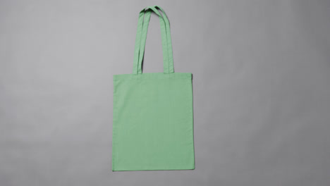 Close-up-of-green-bag-on-grey-background,-with-copy-space,-slow-motion
