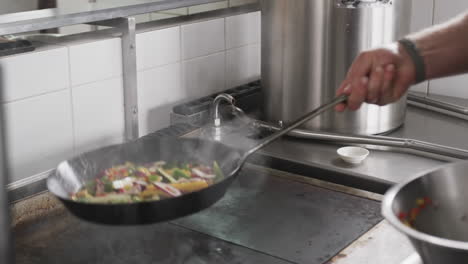 Caucasian-male-chef-frying-vegetables-in-a-pan-in-kitchen,-slow-motion