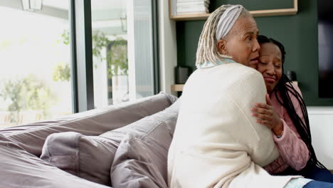 Glückliche-Afroamerikanische-Senior-Mutter-Und-Erwachsene-Tochter-Sitzen-Auf-Der-Couch-Und-Umarmen-Sich,-Zeitlupe