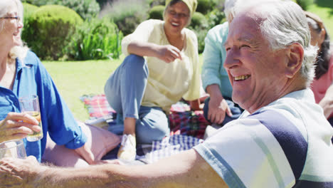 Happy-senior-caucasian-man-laughing-at-a-picnic-with-diverse-friends-in-sunny-garden,-slow-motion