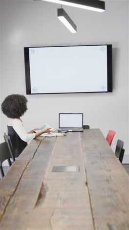 Vertical-video-of-biracial-casual-businesswoman-having-video-call-in-office-meeting-room,-copy-space