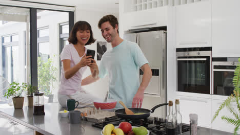 Video-of-happy-diverse-couple-using-smartphone-in-kitchen