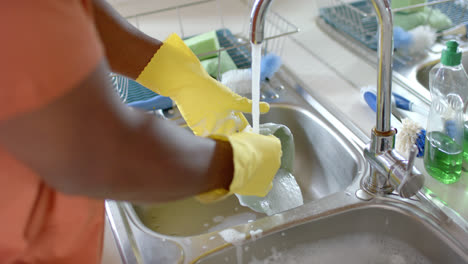 Mid-section-of-african-american-man-washing-dishes-in-bright-kitchen,-slow-motion