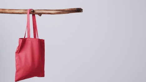 A-red-tote-bag-hangs-from-a-wooden-stick-against-a-plain-background,-with-copy-space