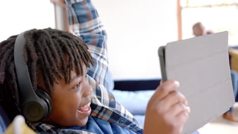 Happy-african-american-boy-with-headphones-using-tablet-lying-on-floor-at-home,-slow-motion