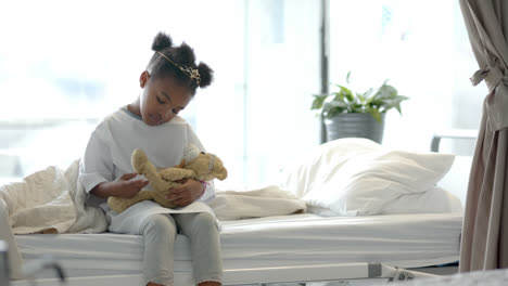 African-american-girl-holding-mascot-in-hospital-bed,-slow-motion