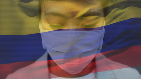 Animation-of-waving-colombia-flag-against-portrait-of-asian-woman-in-face-mask-on-the-street