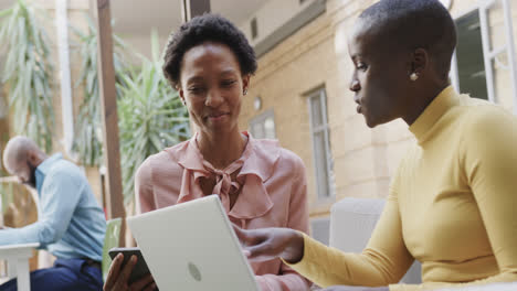 Two-happy-african-american-businesswomen-talking,-laughing-and-using-laptop-outdoors,-in-slow-motion