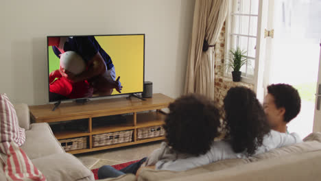 Biracial-family-watching-tv-with-diverse-male-rugby-players-playing-on-screen