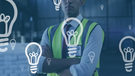 Animation-of-bulb-icons-floating-on-portrait-of-biracial-male-worker-with-arms-crossed-at-warehouse
