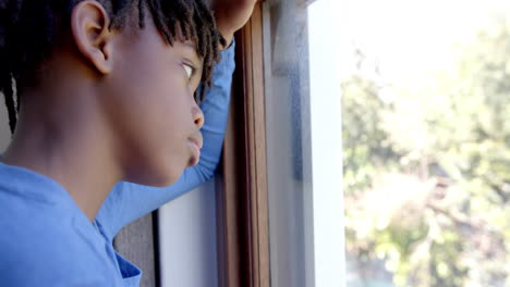 Thoughtful-african-american-boy-looking-through-window-at-home,-slow-motion