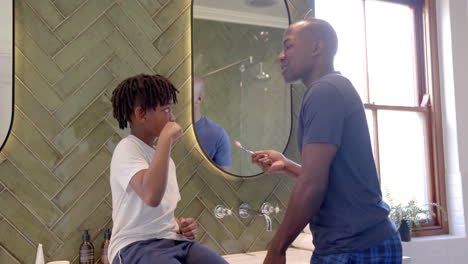 African-american-father-and-son-brushing-teeth-in-bathroom-at-home,-slow-motion