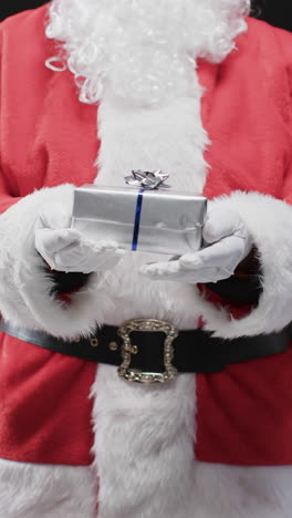 Vertical-video-of-santa-claus-holding-christmas-present-with-copy-space