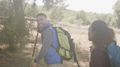 Happy-african-american-couple-hiking-with-trekking-poles-in-forest,-slow-motion