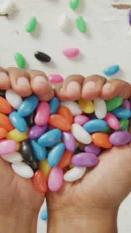 Video-of-overhead-view-of-biracial-man-holding-multi-coloured-sweets-over-white-rustic-background