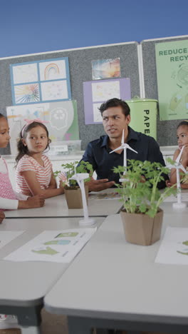 Vertical-video-of-happy-diverse-male-teacher-and-schoolchildren-with-ecology-models-in-slow-motion