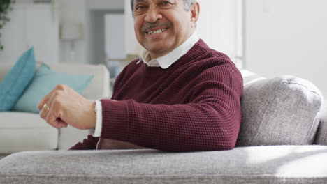 Video-portrait-of-senior-biracial-man-in-living-room-sitting-on-couch-smiling-to-camera