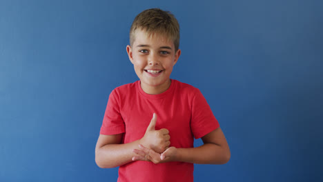 Happy-caucasian-boy-using-sign-language-on-blue-background,-slow-motion