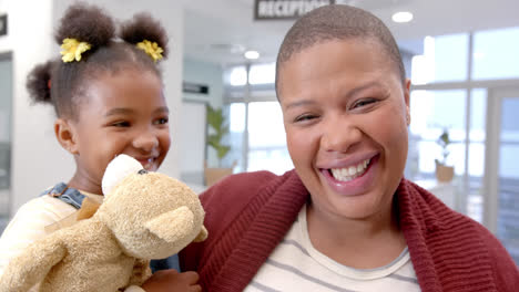 Portrait-of-happy-african-american-mother-holding-daughter-with-mascot-in-hospital,-slow-motion