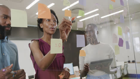 African-american-colleagues-brainstorming,-making-notes-on-glass-wall-in-office-in-slow-motion