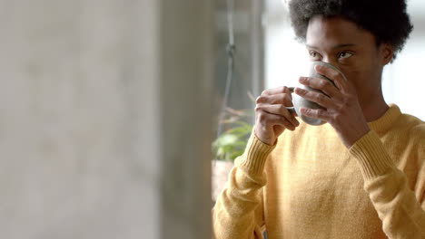 African-american-man-drinking-coffee-and-looking-through-window-at-home,-slow-motion,-copy-space