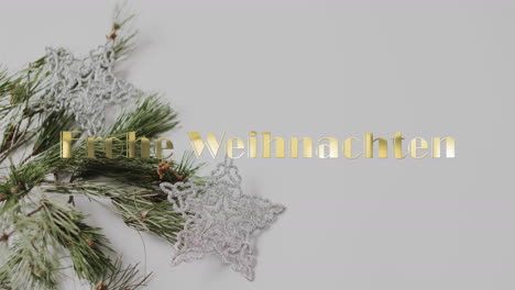 Frohe-weihnachten-text-in-gold-over-christmas-tree-branch-and-star-decorations-on-grey-background