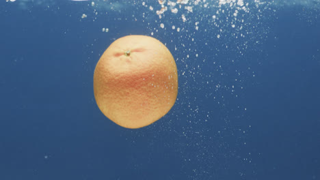 Video-of-orange-falling-into-water-with-copy-space-on-blue-background
