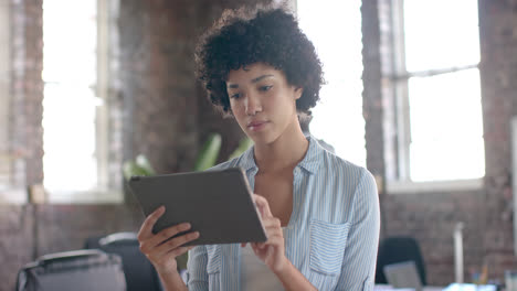 Portrait-of-happy-biracial-casual-businesswoman-using-tablet-in-office-in-slow-motion