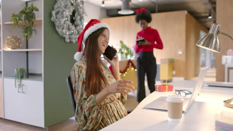 Happy-biracial-casual-businesswoman-with-christmas-hat-talking-on-smartphone-in-office,-slow-motion