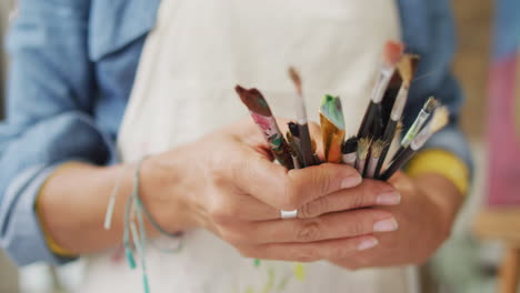 Artist's-hands-holding-a-variety-of-paintbrushes,-with-copy-space