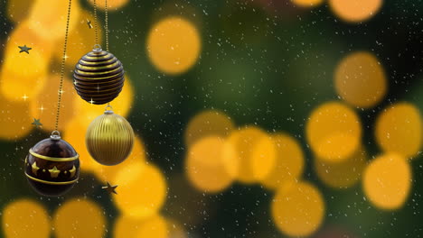 Swinging-black-and-gold-christmas-baubles,-falling-snow-and-orange-bokeh-lights-on-dark-background