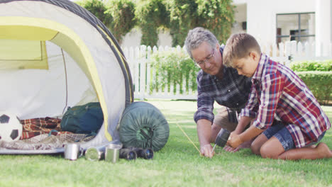 Happy-caucasian-grandfather-and-grandson-pitching-tent-together-in-garden,-slow-motion