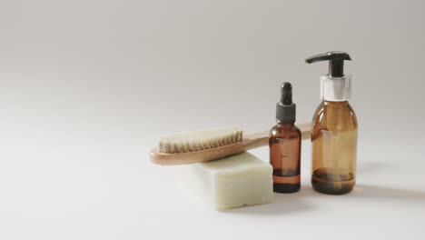 Close-up-of-glass-bottles-with-pumps,-soap,-brush-and-copy-space-on-white-background