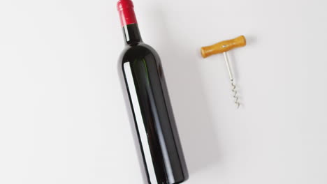A-bottle-of-red-wine-lies-next-to-a-corkscrew-on-a-white-surface