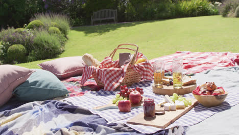 Picnic-hamper,-food-and-drinks-laid-out-on-blankets-in-a-sunny-garden,-slow-motion
