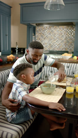 Vertical-video-of-happy-african-american-father-and-son-having-breakfast,-in-slow-motion