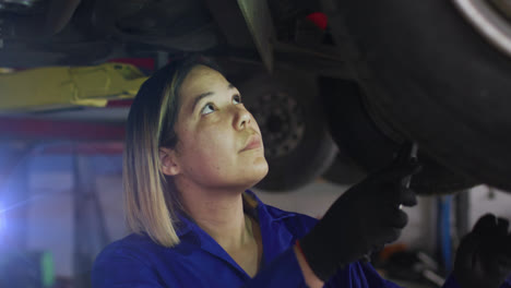 Animation-of-asian-female-mechanic-standing-under-car-examining-vehicle-with-hand-tool-in-garage