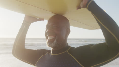 Feliz-Hombre-Afroamericano-Mayor-Caminando-Y-Sosteniendo-Tabla-De-Surf-En-La-Playa,-En-Cámara-Lenta