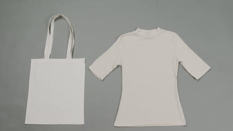 Nahaufnahme-Einer-Weißen-Tasche-Und-Eines-T-Shirts-Auf-Grauem-Hintergrund,-Mit-Kopierraum,-Zeitlupe