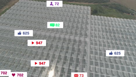 Animation-of-social-media-icons-floating-against-aerial-view-of-solar-panels-in-grassland