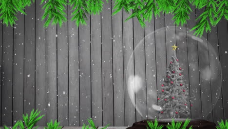 Animation-of-branch-and-snow-falling-over-christmas-tree-in-a-snowglobe-against-wooden-background