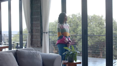 Thoughtful-biracial-woman-looking-through-window-at-home,-slow-motion,-copy-space