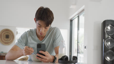 Asiatischer-Junge-Benutzt-Smartphone-Beim-Frühstück-Im-Wohnzimmer-Zu-Hause
