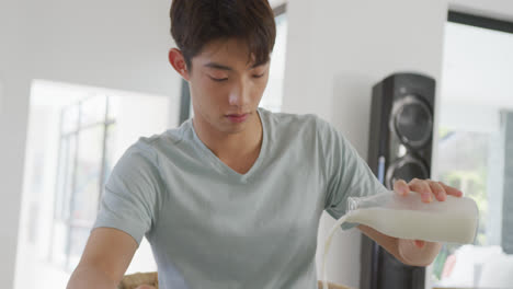 Asian-boy-pouring-milk-in-his-cereal-bowl-at-home